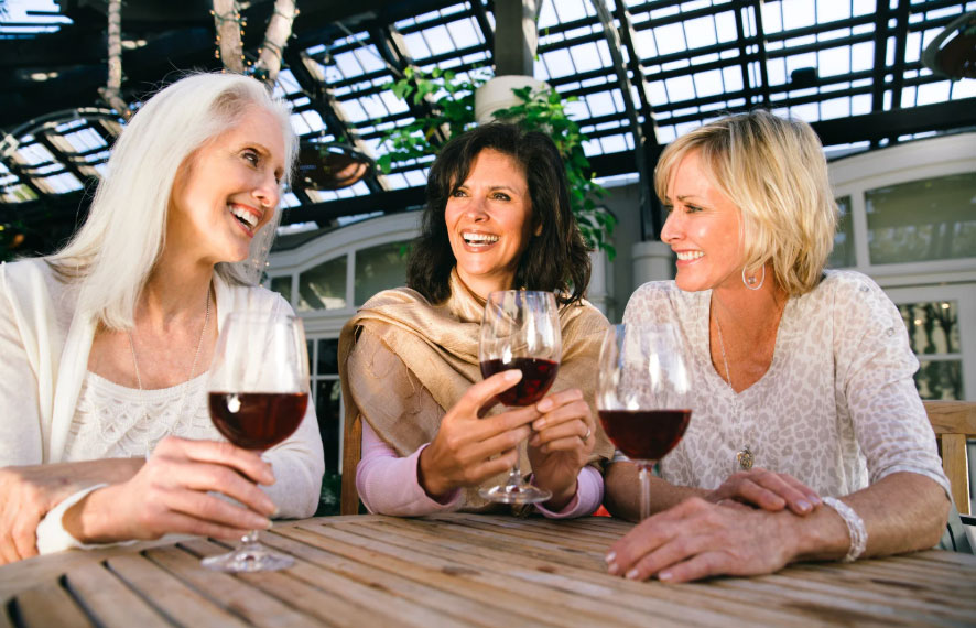 Three older women sitting together and drinking red wine and laughing