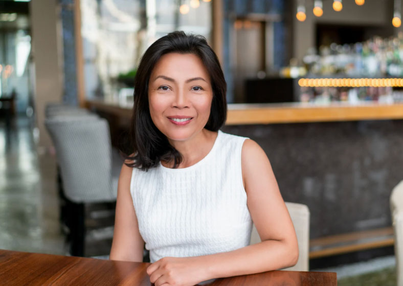 Image of an older Asian woman with shoulder length dark hair wearing a white, sleeveless shirt